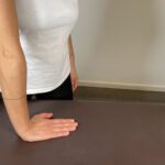 Frau legt ihre Hand mit nach vorne zeigenden Fingern flach auf eine Tischoberfläche zur Dehnung der Handgelenksbeuger.