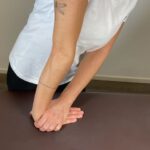 Frau vertieft die Dehnung der Handgelenksbeuger durch weiteres Vorbeugen des Körpers.