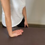 Hand- und Unterarmdehnung: Frau legt ihre Handfläche mit nach hinten zeigenden Fingern auf eine Tischoberfläche.