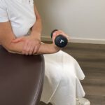 Frau hebt die Hantel kontrolliert nach oben, um die Handgelenksbeugemuskulatur zu kräftigen.