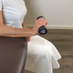 Frau hebt die Hantel kontrolliert nach oben, um die Handgelenksstreckmuskulatur zu kräftigen.